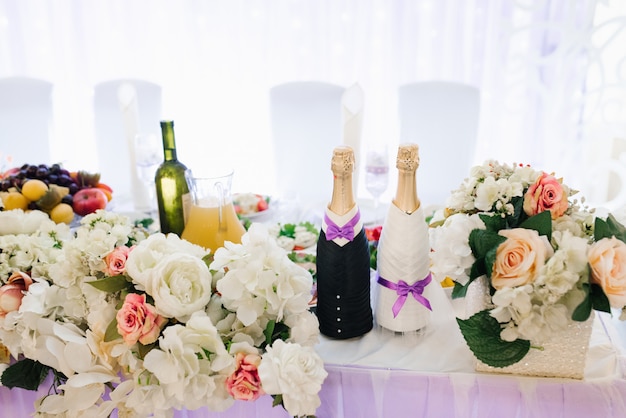 Deux bouteilles de champagne, habillées comme la mariée et le marié, se tenaient sur la table de fête de mariage en fleurs