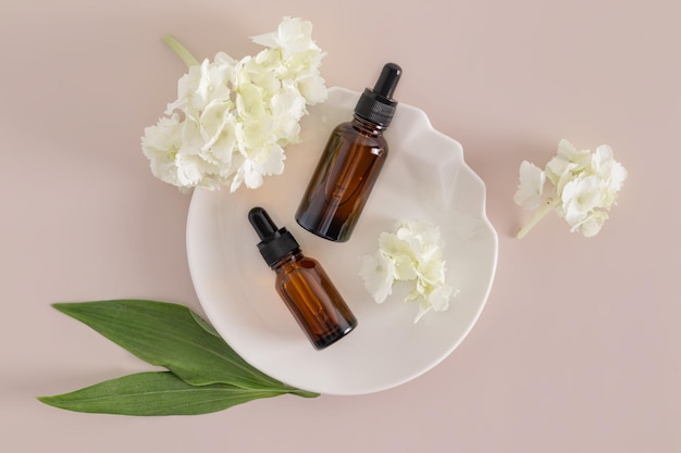 Deux bouteilles de cosmétiques avec un produit de soin de la peau du visage et du corps anti-vieillissement sur une plaque abstraite blanche avec des fleurs Emballage avec une étiquette blanche pour la marque