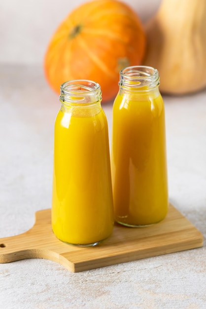 Deux bouteilles de jus de citrouille sur une planche à découper en bois Citrouille entière crue Automne Boisson diététique saine