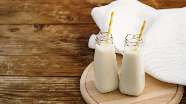 Deux bouteilles de lait rustique biologique sur table en bois avec des pailles en papier jaune. Copier l'espace