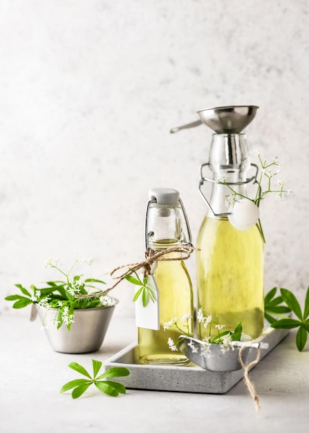 Deux bouteilles en verre de sirop d'aspérule sucré fait maison dans un plateau gris avec des feuilles vertes fraîches