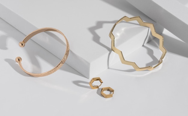 Deux bracelets et boucles d'oreilles dorés de forme géométrique moderne sur un podium blanc avec espace de copie