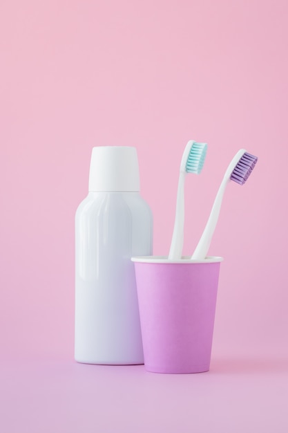 Deux brosses à dents dans une tasse rose et un rince-bouche dans une bouteille, concept d'hygiène buccale.