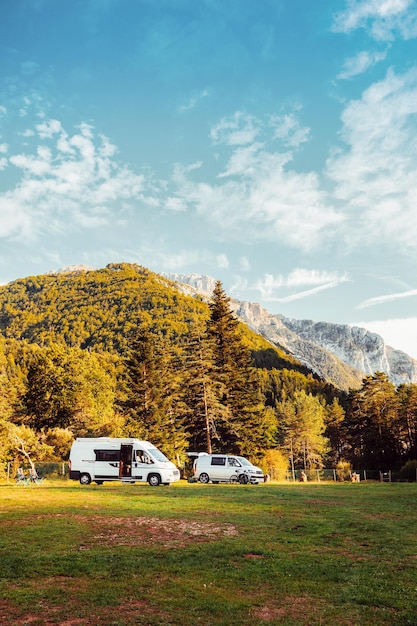 Deux camping-cars dans un camping avec une vue imprenable sur la forêt et les montagnes pendant le coucher du soleil Voyage en van et aventure estivale en plein air Concept de style de vie nomade