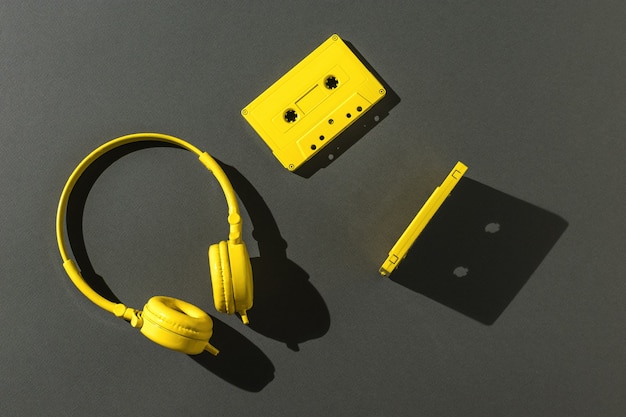 Deux cassettes avec bande magnétique et casque jaune en lumière vive sur fond gris. Tendance de couleur. Matériel vintage pour écouter de la musique. Mise à plat.