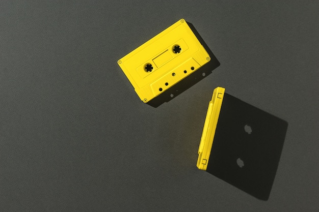 Deux cassettes jaunes avec bande magnétique en lumière vive sur fond noir. Mise à plat.