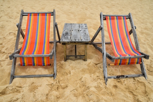 Deux chaises de salon en toile colorées vides et table en bois sur la plage de sable