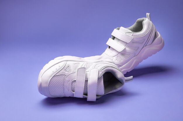 Deux chaussures de course pour enfants blanches avec fermetures velcro pour des chaussures faciles pour enfants isolées sur un fond mauve ...