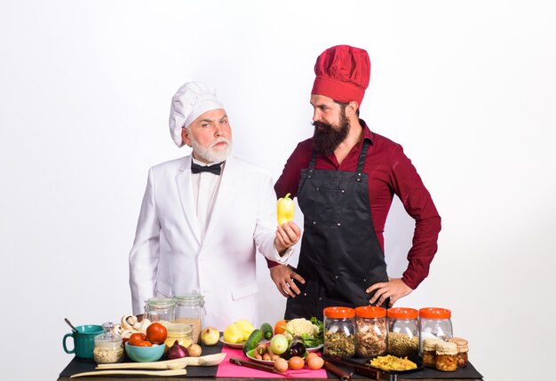 Deux chefs culinaires professionnels se tiennent près de la table avec des chefs d'hommes barbus de légumes en uniforme prêt