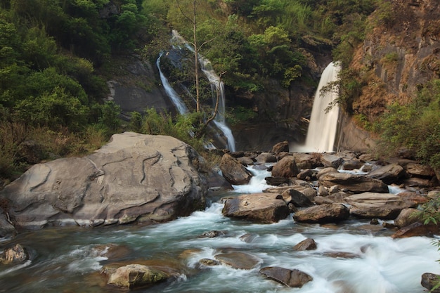 Deux chutes d'eau dans une petite vallée paisible avec de l'eau turquoise brillante coulant entre de grosses pierres