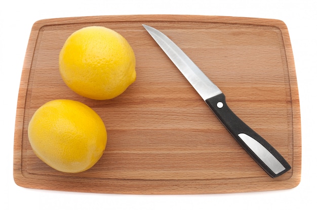 Deux citron frais jaune avec un couteau sur une planche à découper en bois.