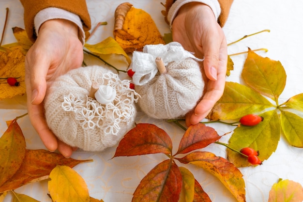 Deux citrouilles tricotées blanches sur fond blanc avec des feuilles d'automne