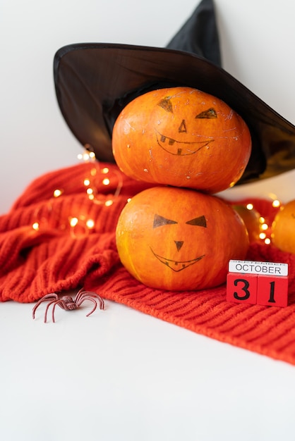 Photo deux citrouilles avec un visage peint dans un chapeau, une araignée, un calendrier en bois sur un pull rouge. concept de vacances du 31 octobre, halloween. beau bokeh sur le fond.