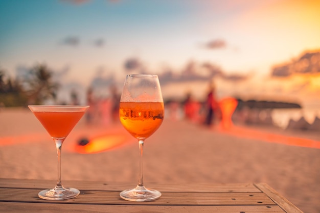 Deux cocktails avec des fêtards flous sur la plage et un ciel coloré au coucher du soleil en arrière-plan. Le luxe