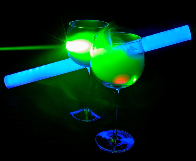 Deux cocktails fumés avec un tube néon et un laser vert, sur fond sombre.