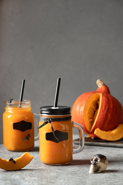 Deux cocktails d'Halloween avec du jus de citrouille garnissent le crâne et les araignées pour une fête festive sur fond gris