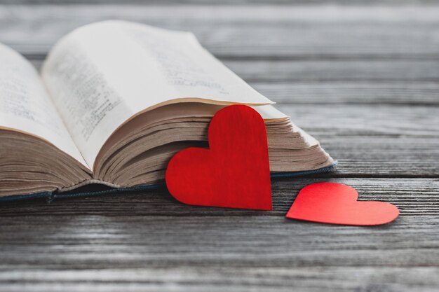 Deux coeurs de papier rouge et livre ouvert sur la table en bois