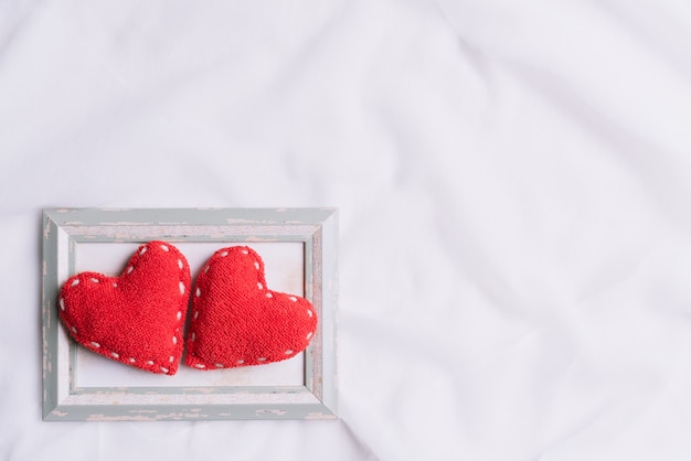 Deux coeurs rouges dans le cadre photo sur fond de tissu blanc.