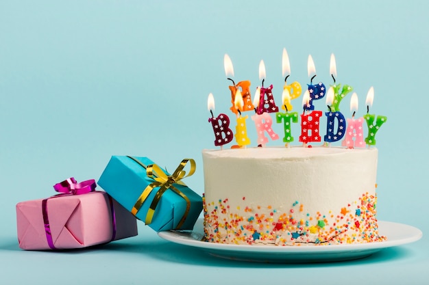 Photo deux coffrets cadeaux près du gâteau avec des bougies joyeux anniversaire sur fond bleu