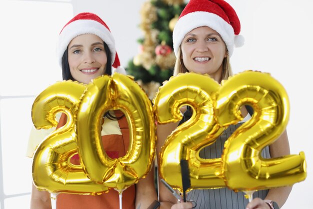 Deux coiffeuses souriantes tiennent des numéros sur fond de beauté d'arbre du nouvel an