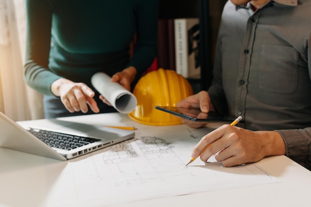 Deux collègues discutant du travail des données et d'une tablette, d'un ordinateur portable avec un projet architectural sur un chantier de construction au bureau du bureau