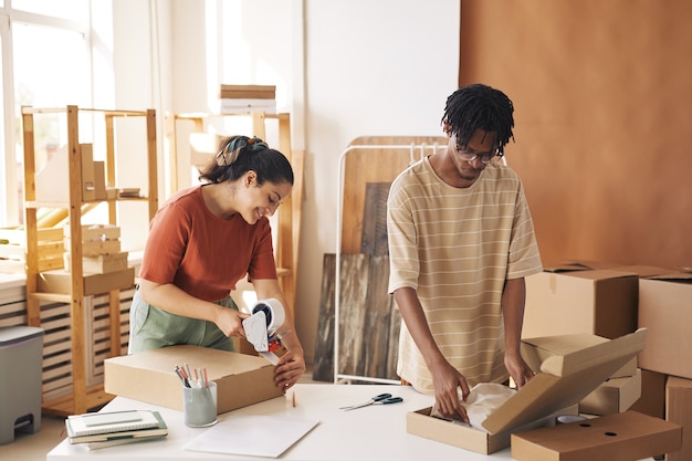 Deux collègues emballant de nouveaux vêtements dans les boîtes en carton à la table de l'entrepôt, ils préparent les colis pour la livraison