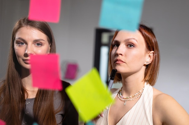 Deux collègues féminines se tiennent devant des autocollants colorés avec des plans d'entreprise