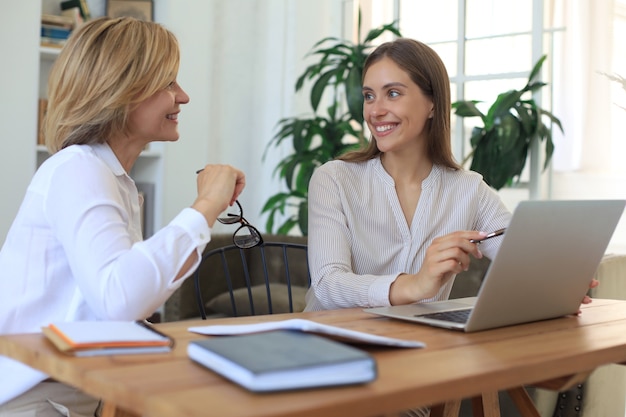 Deux collègues féminines travaillant avec un ordinateur portable et discutant d'un nouveau projet.