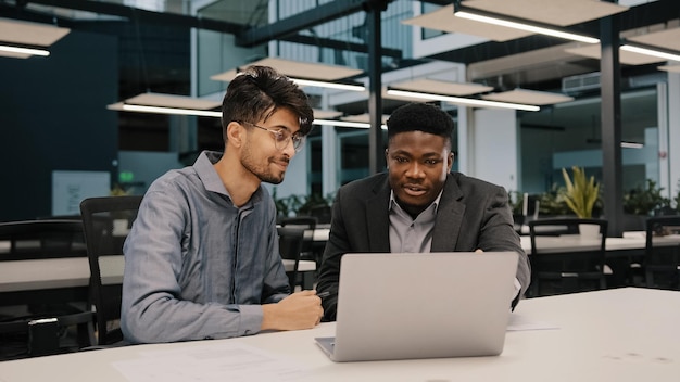 Deux collègues masculins professionnels multiculturels hommes collègues au bureau utilisent un ordinateur portable discuter du projet