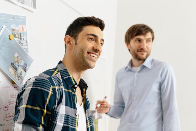 Deux collègues souriants au tableau blanc au bureau