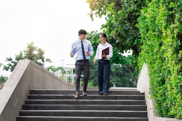 Deux collègues de travail asiatiques à l'extérieur des immeubles de bureaux discutent et commentent leur travail.