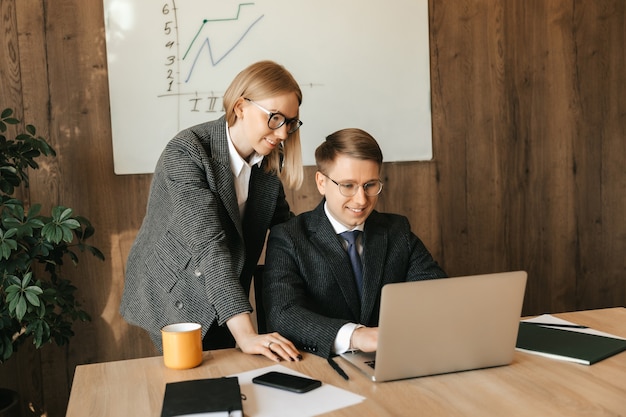 Deux collègues de travail regardent des documents et travaillent sur un ordinateur portable, une secrétaire ou une femme gestionnaire lit un document, femme d'affaires souriante.