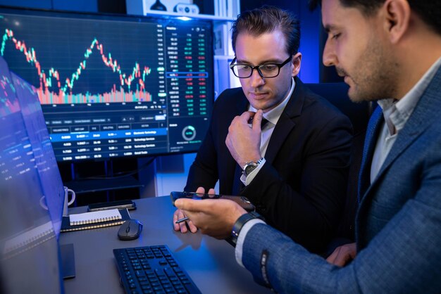 Deux commerçants de bourse discutent de graphique d'investissement dynamique dans le taux de change sur l'écran la nuit Partenaires d'affaires réunion de café sur le marché boursier élevé à la lumière du néon sur le lieu de travail Vendable