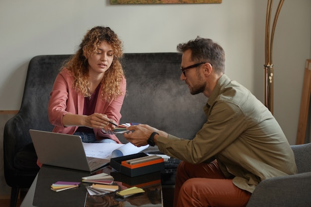 Deux concepteurs assis à la table devant un ordinateur portable et examinant les motifs colorés au bureau