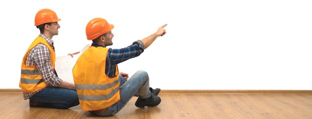 Les deux constructeurs avec un papier sont assis sur le sol sur le fond du mur blanc