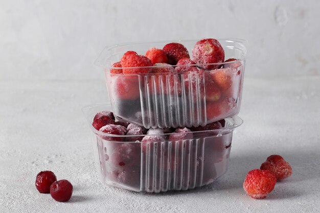 Deux contenants de baies congelées : fraises et cerises sur fond gris clair. Récolte des baies pour l'hiver.