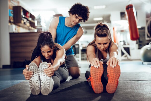 Photo deux copines faisant de l'exercice avec un entraîneur personnel au gymnase.