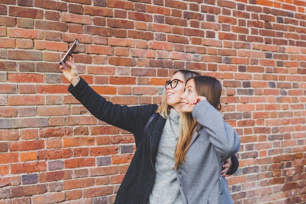 Deux copines hipster prenant une photo de soi pour les réseaux sociaux dans l'amitié de fond de ville urbaine