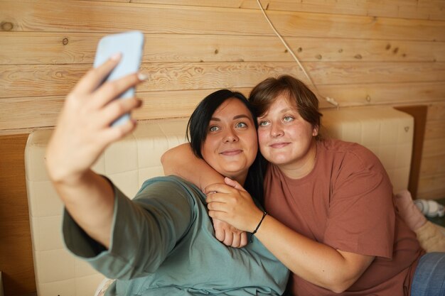 Deux copines s'embrassant et faisant selfie au téléphone tout en se reposant sur le lit