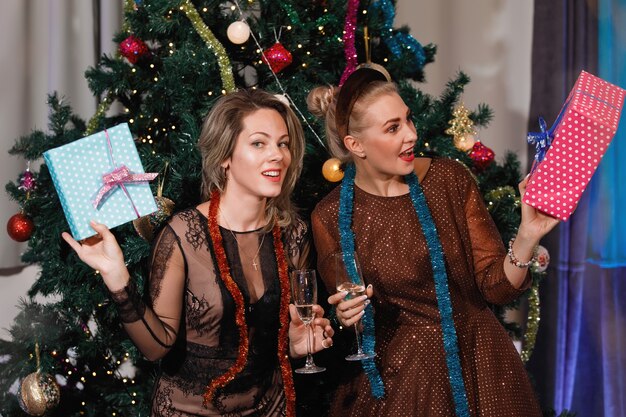 Deux copines s'offrent des coffrets cadeaux près d'un sapin de Noël.