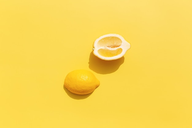 Deux coupes de citron coupées en deux avec une ombre sur une surface jaune