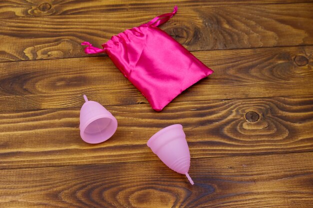 Deux coupes menstruelles en silicone réutilisable rose et un sac en soie sur fond de bois Concept d'hygiène féminine gynécologie et santé