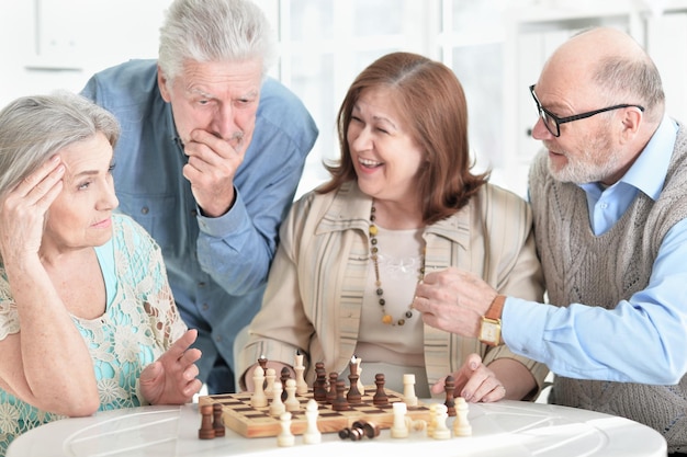 Deux couples âgés assis à table et jouant aux échecs