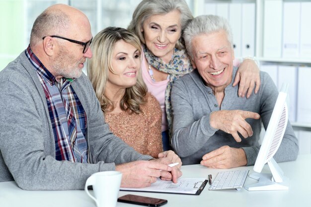 Deux couples âgés assis à table et travaillant avec un ordinateur