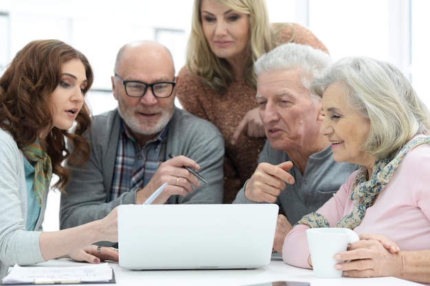 Deux couples âgés parlant avec un consultant assis à table et regardant un ordinateur portable