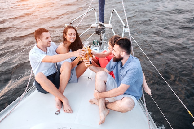 Deux couples assis sur la proue du yacht et acclamations avec de la bière