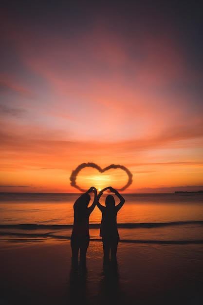 deux couples se tenant par la main pour former une forme de cœur au coucher du soleil sur la plage