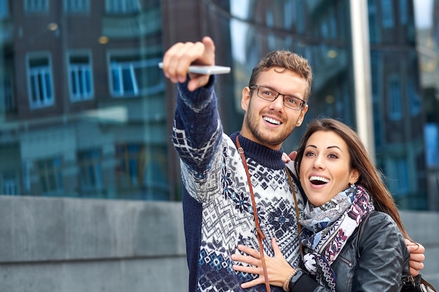 Deux couples de touristes heureux recherchent un emplacement avec un téléphone et une carte et pointent du doigt.