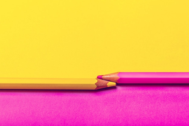 Deux crayons de couleur sur fond rose et jaune.