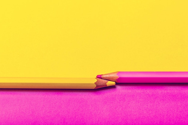 Deux crayons de couleur sur fond rose et jaune